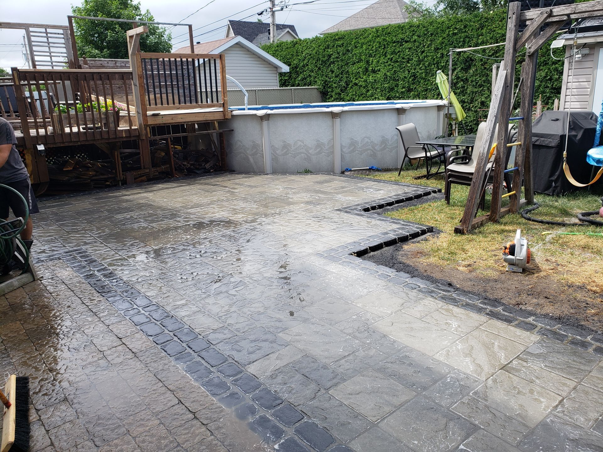Aménagement d'une terrasse arrière avec pavés de brique, terrasse en bois, piscine hors sol et canaux de drainage.