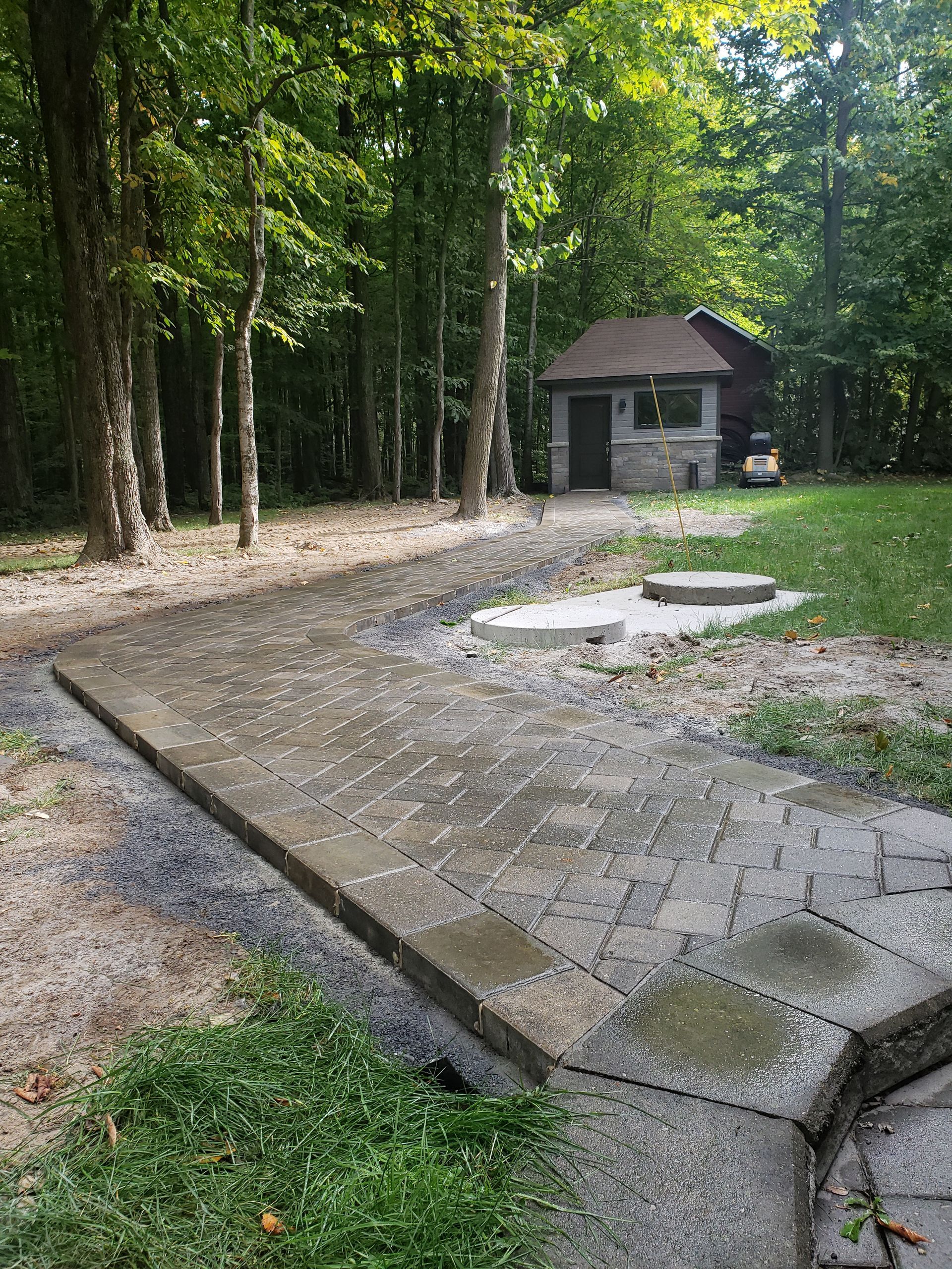 Un chemin de briques mène à un petit bâtiment en pierre situé dans un cadre boisé.