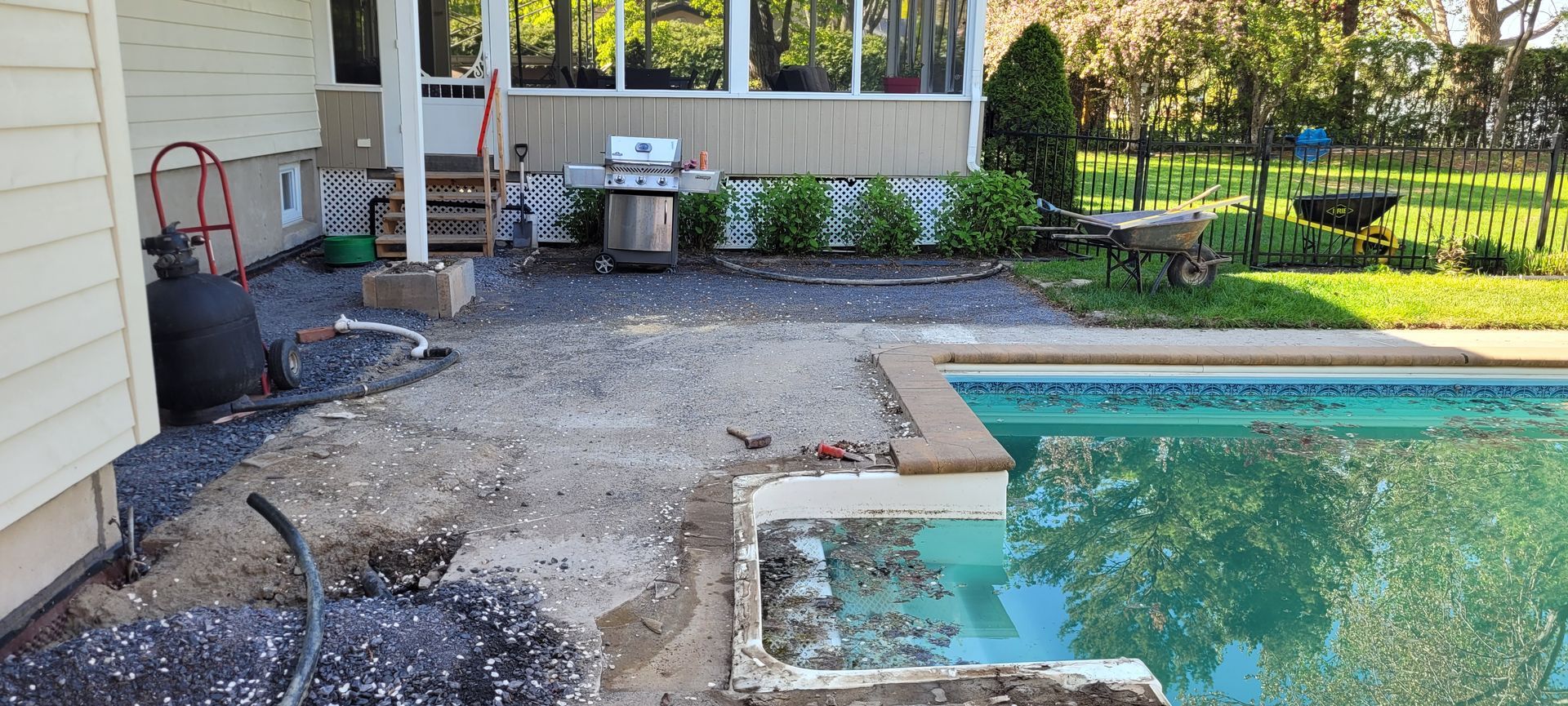 Jardin avec piscine, terrasse et barbecue ; en cours de rénovation. Gravier et débris éparpillés autour de la piscine.