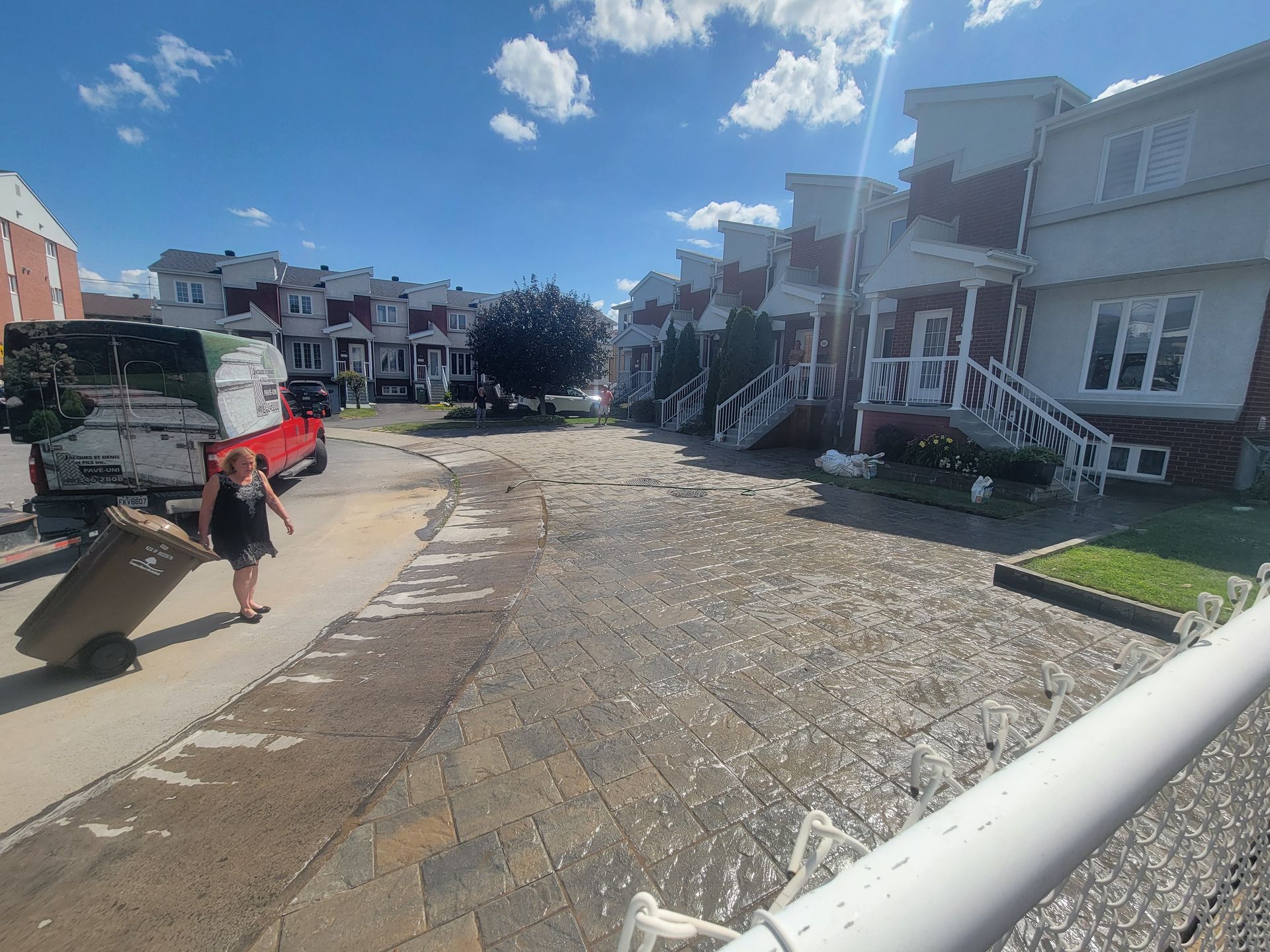 Une femme tire une poubelle dans une rue détrempée bordée de maisons inondées. Un camion est stationné à proximité.