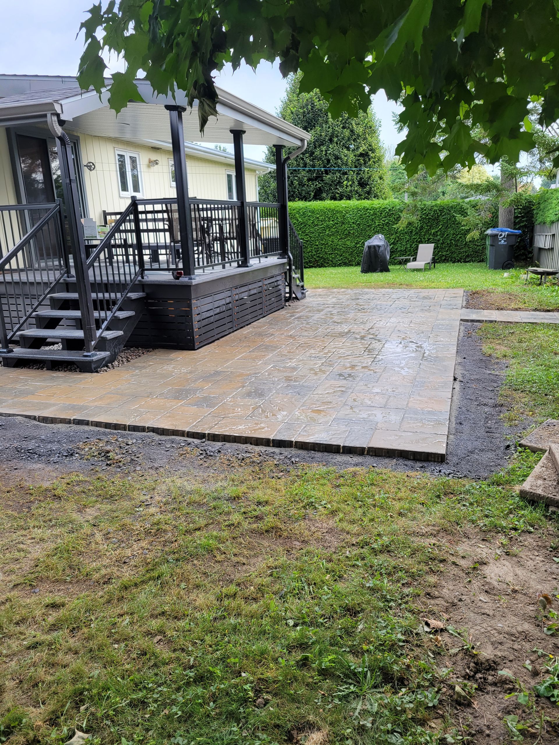 Patio avec marches menant à une terrasse, bordée de gravier et de gazon.
