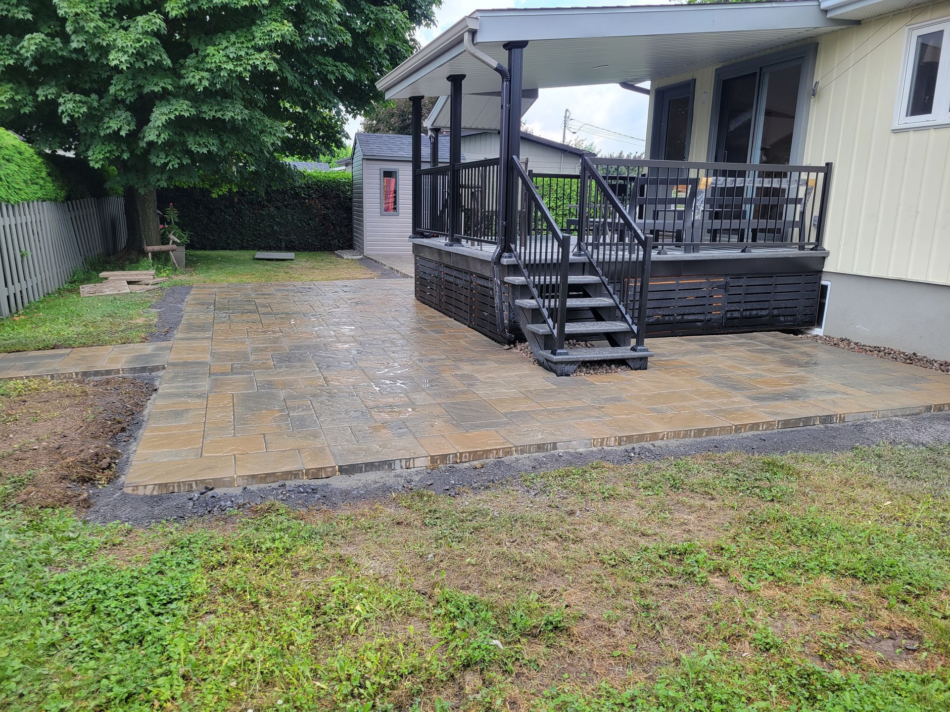 Terrasse et patio en pavés gris foncé jouxtent une maison jaune clair. Un escalier noir mène à la terrasse.
