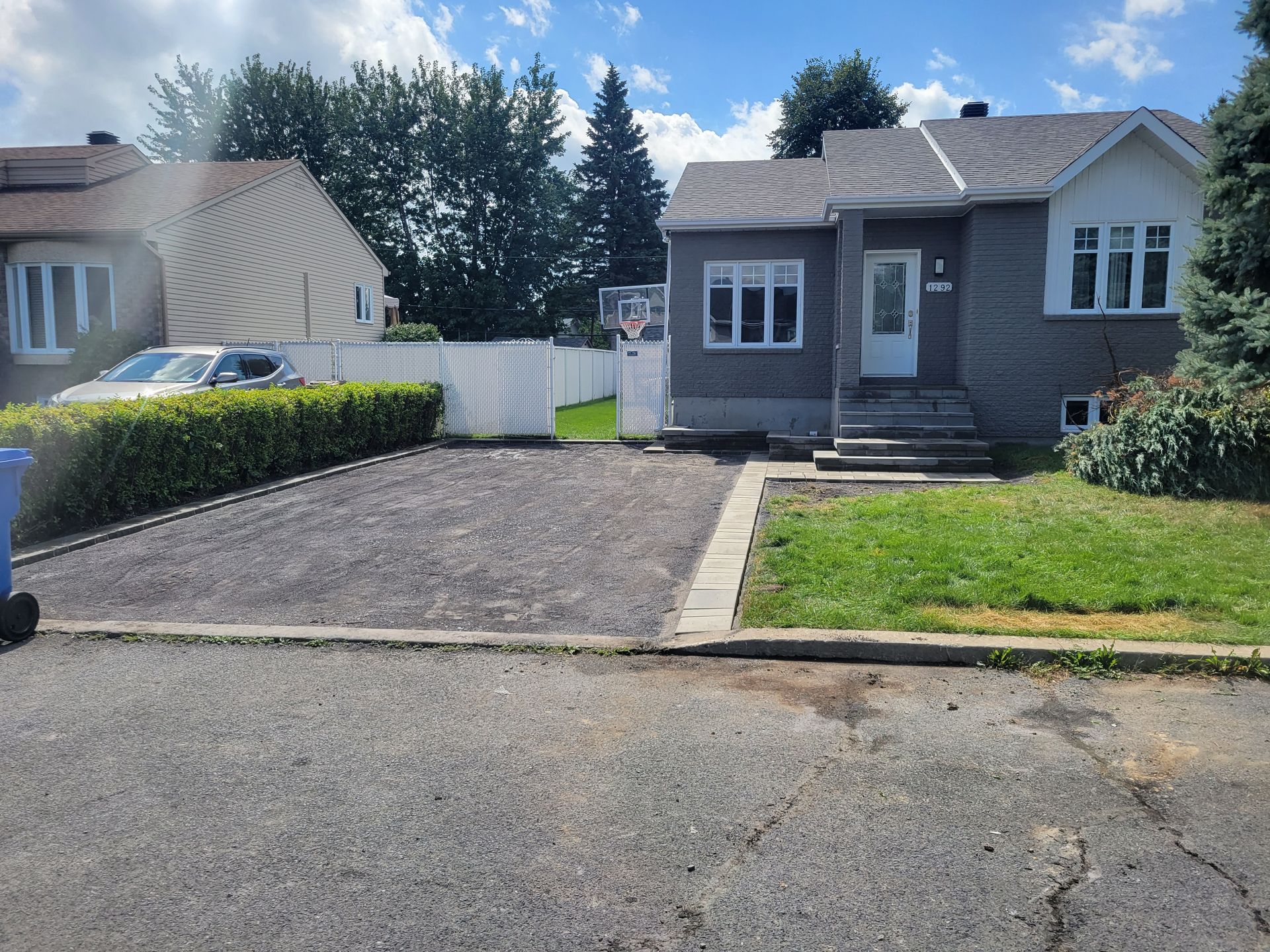 Une maison grise avec une petite allée, devant laquelle se trouve une pelouse. Une autre maison est visible sur la gauche.