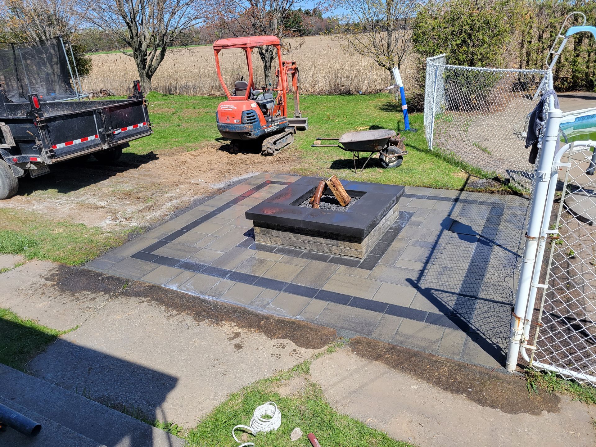 Foyer extérieur sur une terrasse en pierre avec mini-pelle, camion et clôture en grillage.