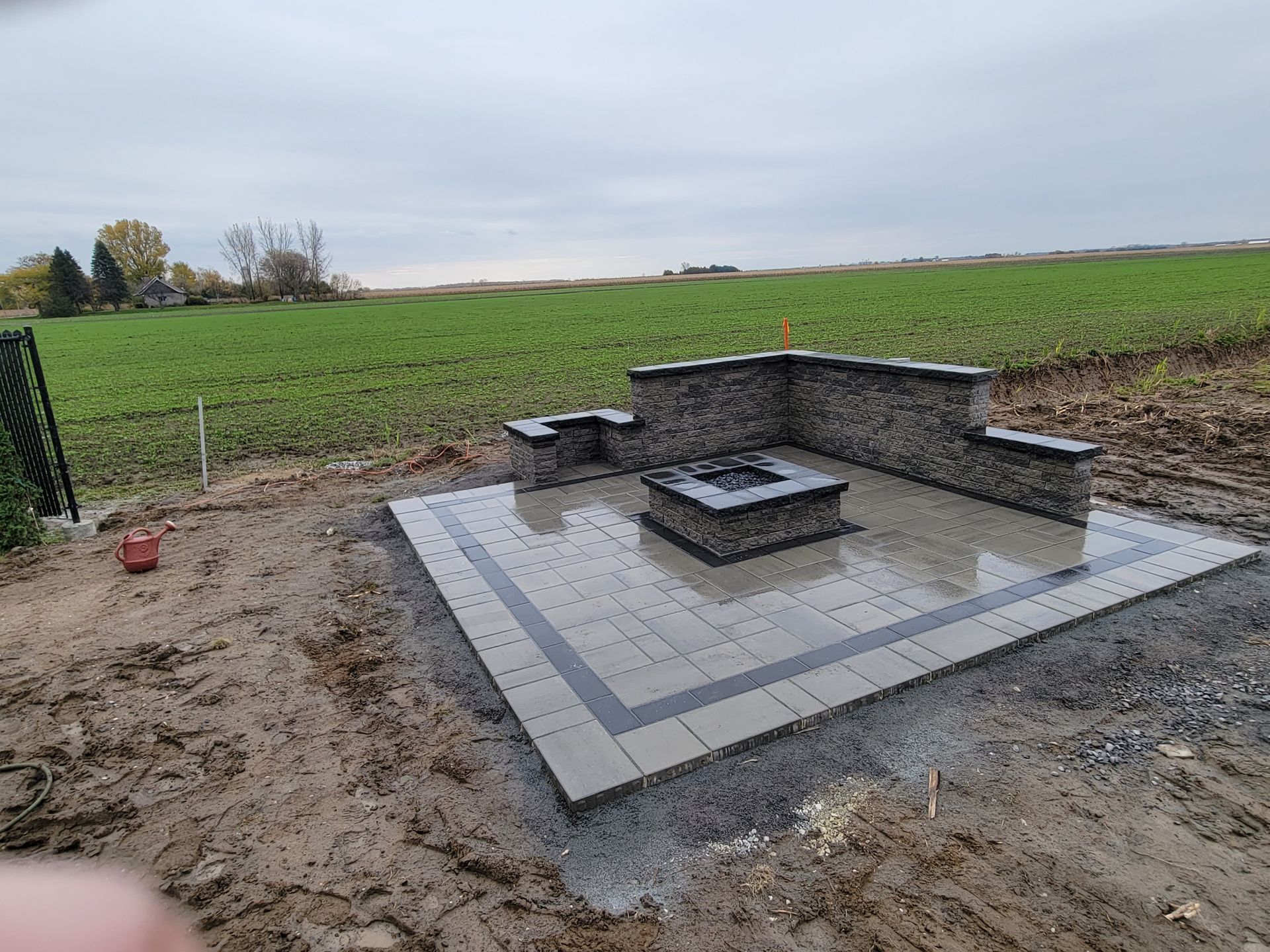 Terrasse avec foyer, sièges en pierre et pavage dans un champ sous un ciel couvert.