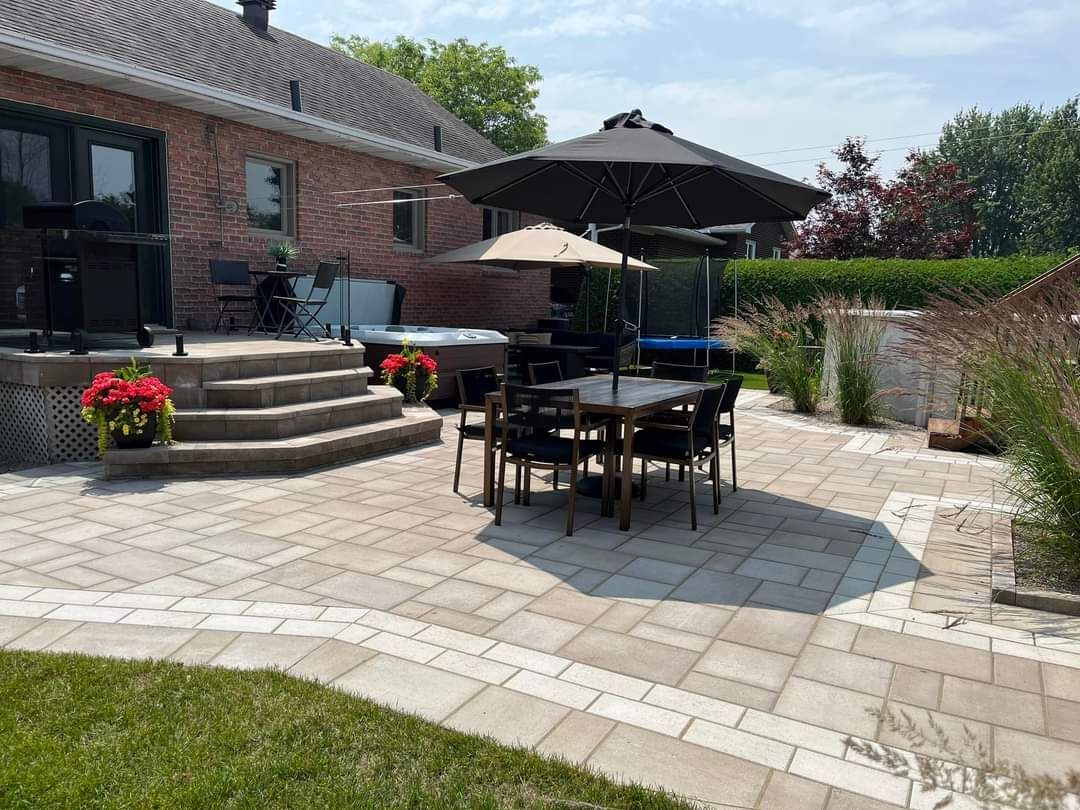 Terrasse avec table, chaises, parasols et jacuzzi près d'une maison en briques par une journée ensoleillée.