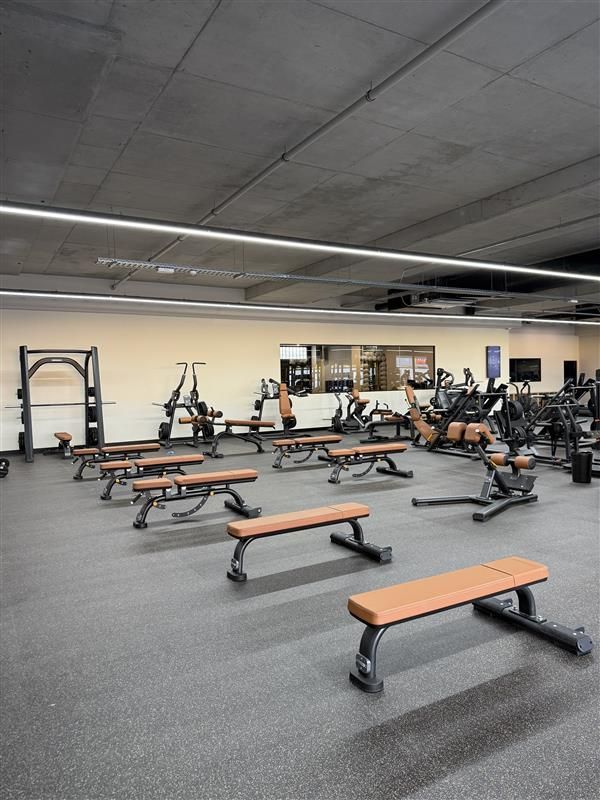 An interior view of a gym featuring rows of brown weight benches and various strength training equipment.