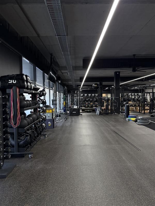 Empty gym with a rack of heavy balls and kettlebells on the left, leading to a long, open workout area with lighting.