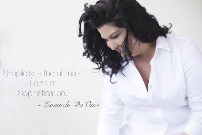 Woman in a white blouse looking downward against a light background with a faint quote on the left