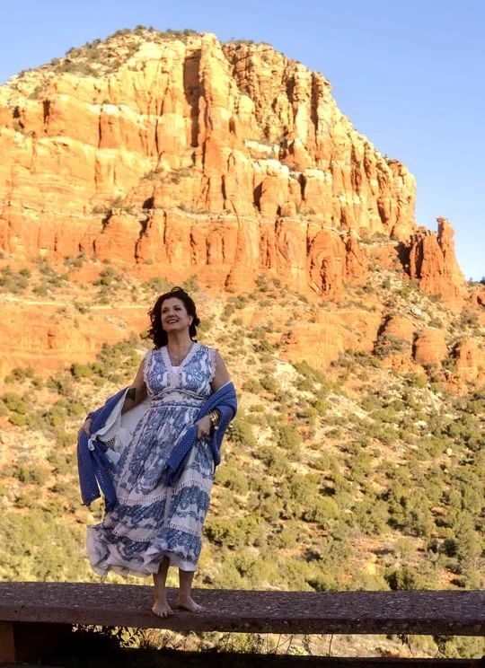 Woman in white outfit and sunglasses posing outdoors with the name “ANN MARIA” below.