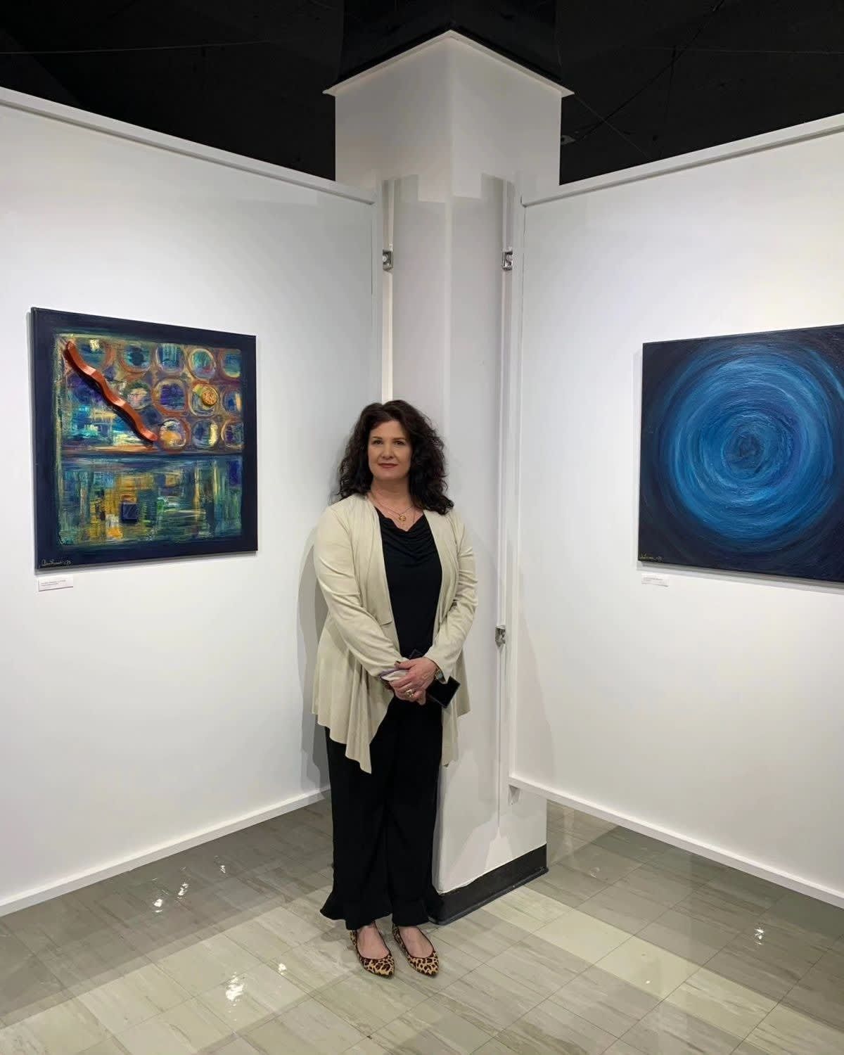 Woman standing in an art gallery between two colorful framed paintings.