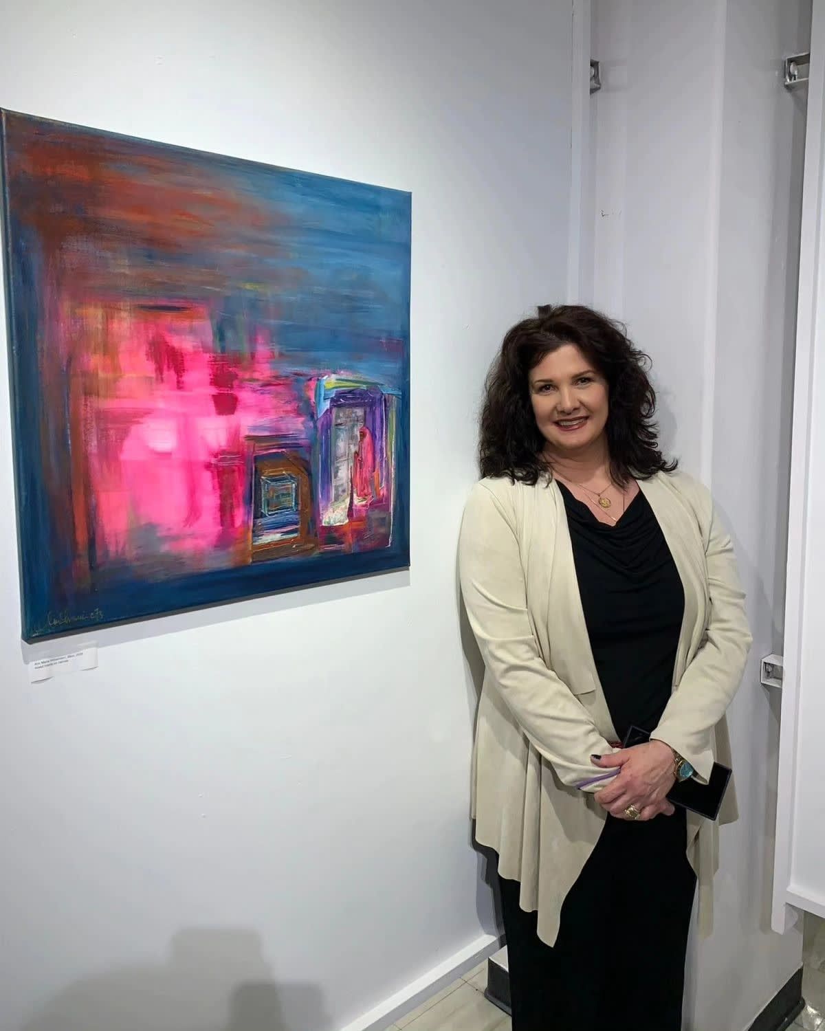 Woman standing beside a colorful abstract painting in a gallery hallway