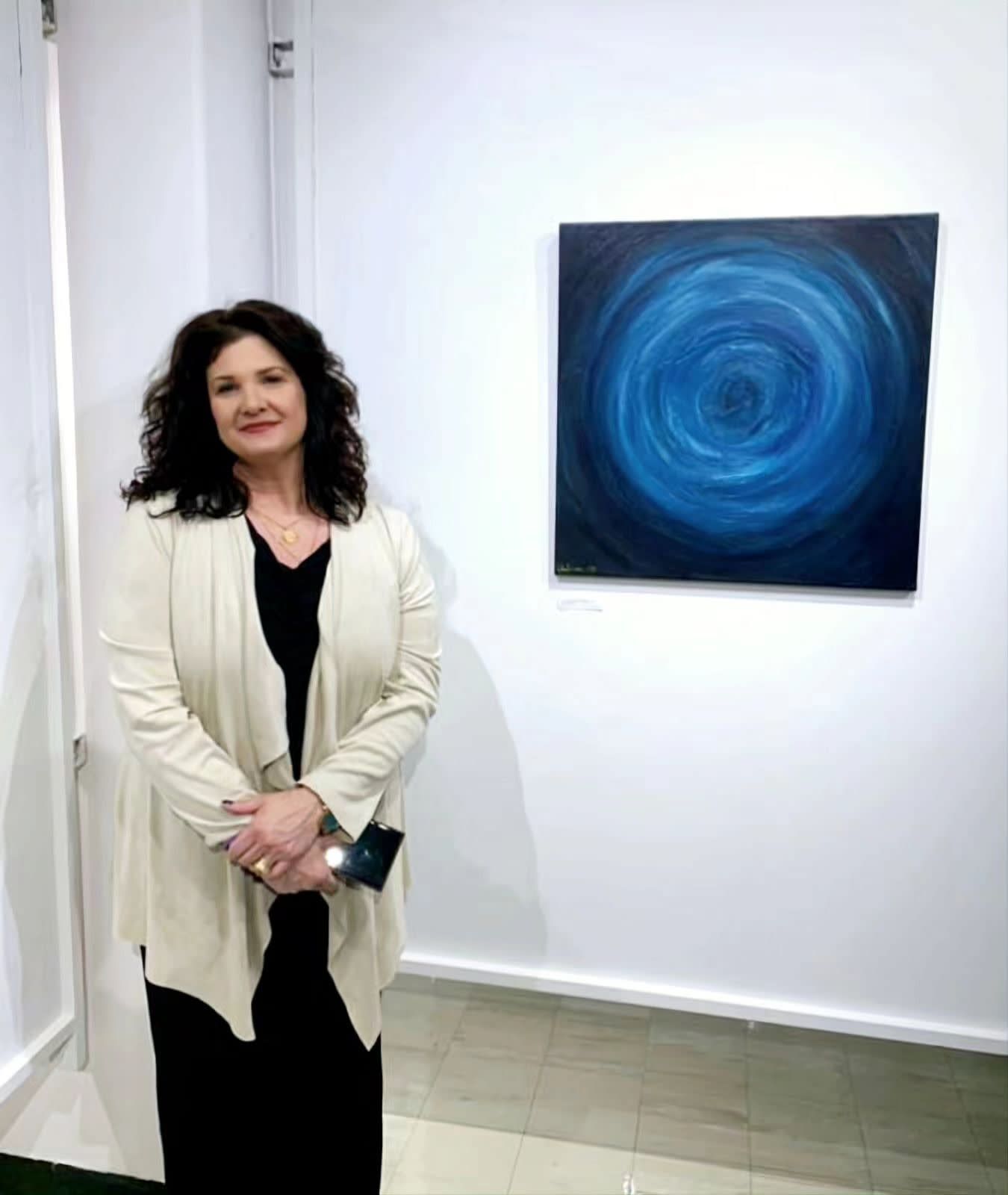 Woman standing by a blue abstract painting in a white gallery space.
