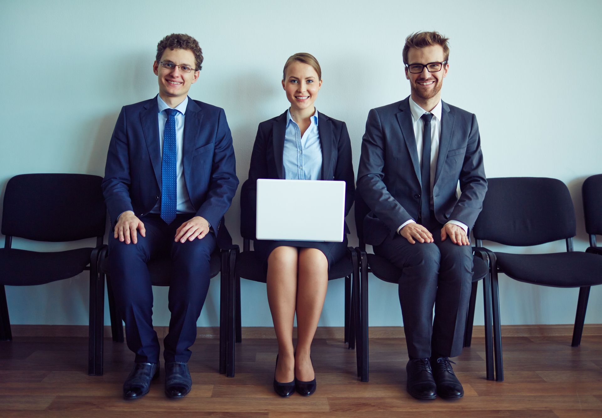 three people are sitting in chairs waiting for a job interview .