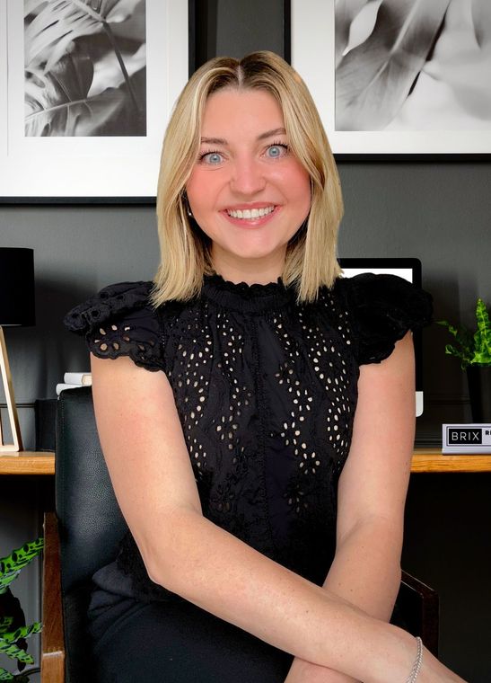 A woman is sitting at a desk with a laptop and a vase of flowers.