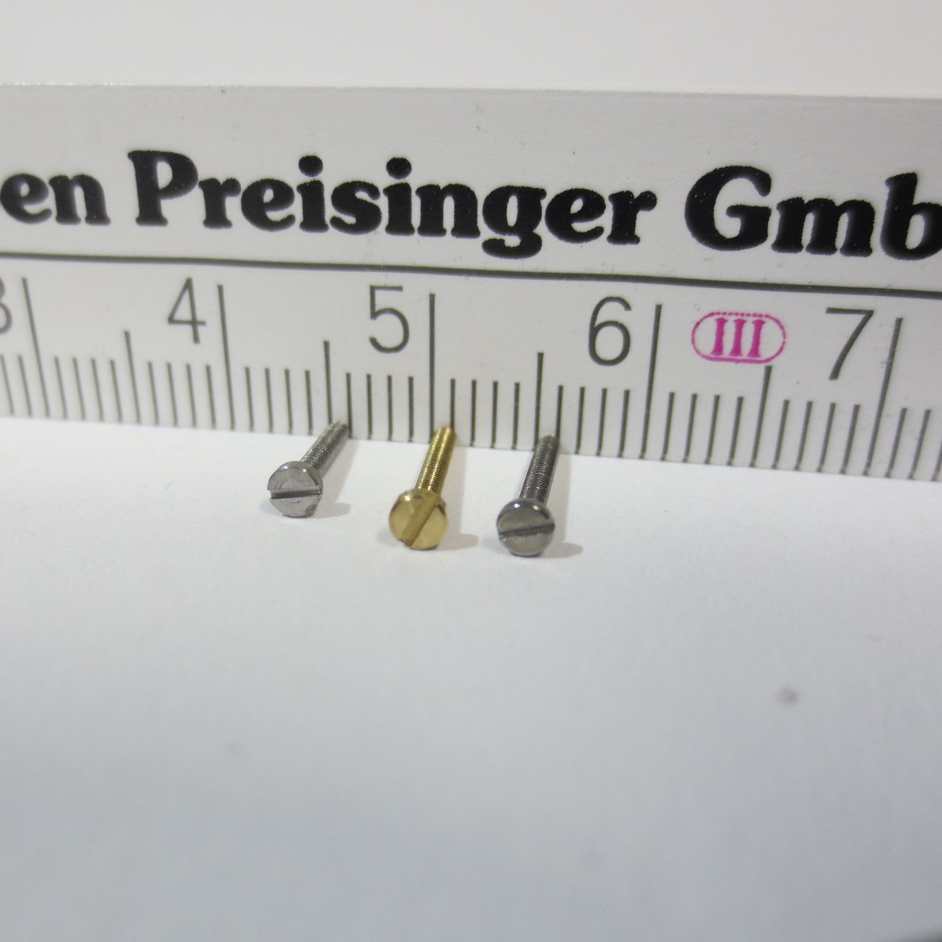 Drei Schrauben liegen neben einem Lineal mit der Aufschrift Schrauben-Preisinger GmbH