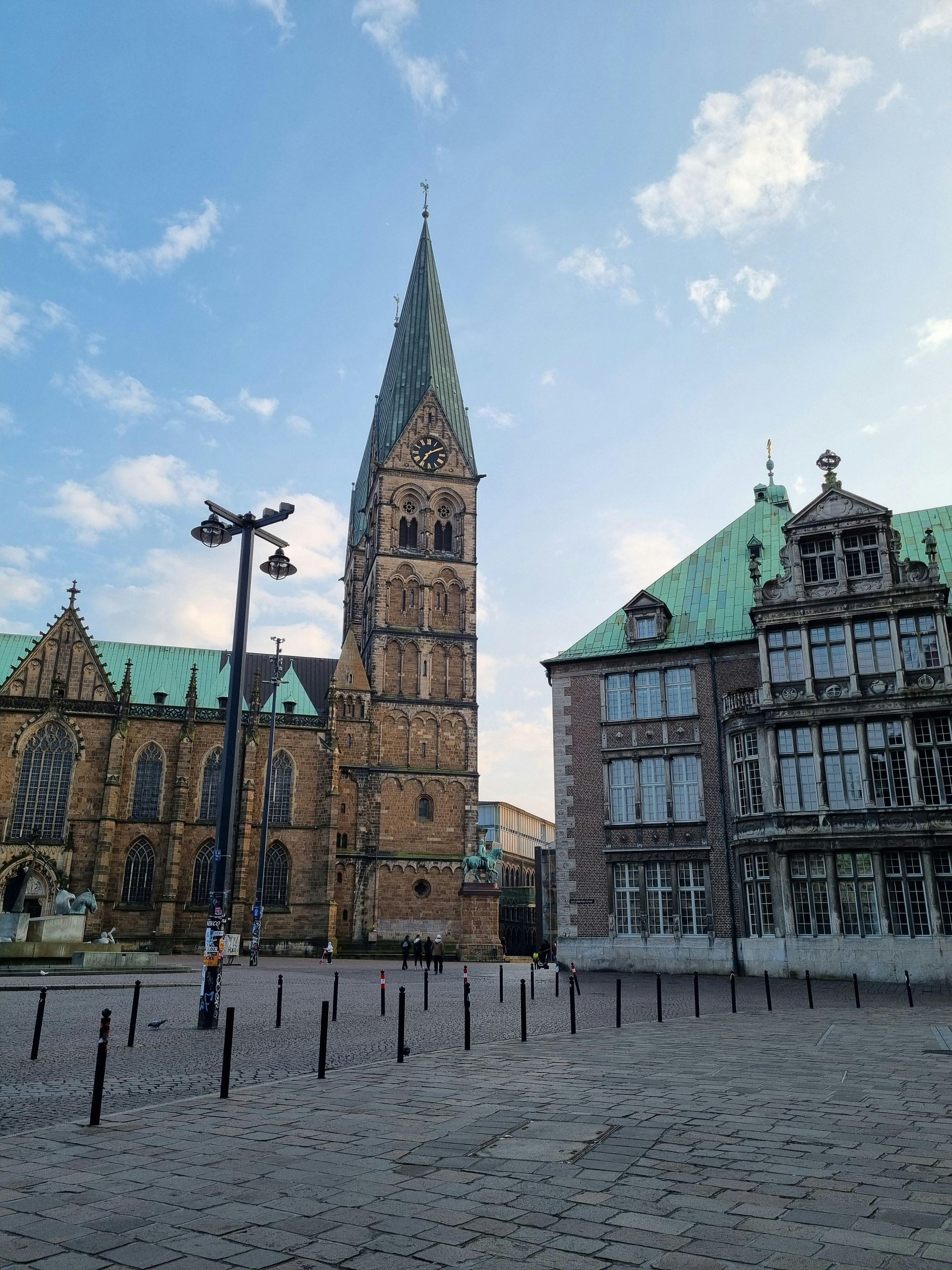 Bremen, Germany: Stone buildings, a tall church tower, and a cobblestone square under a partly cloudy sky.
