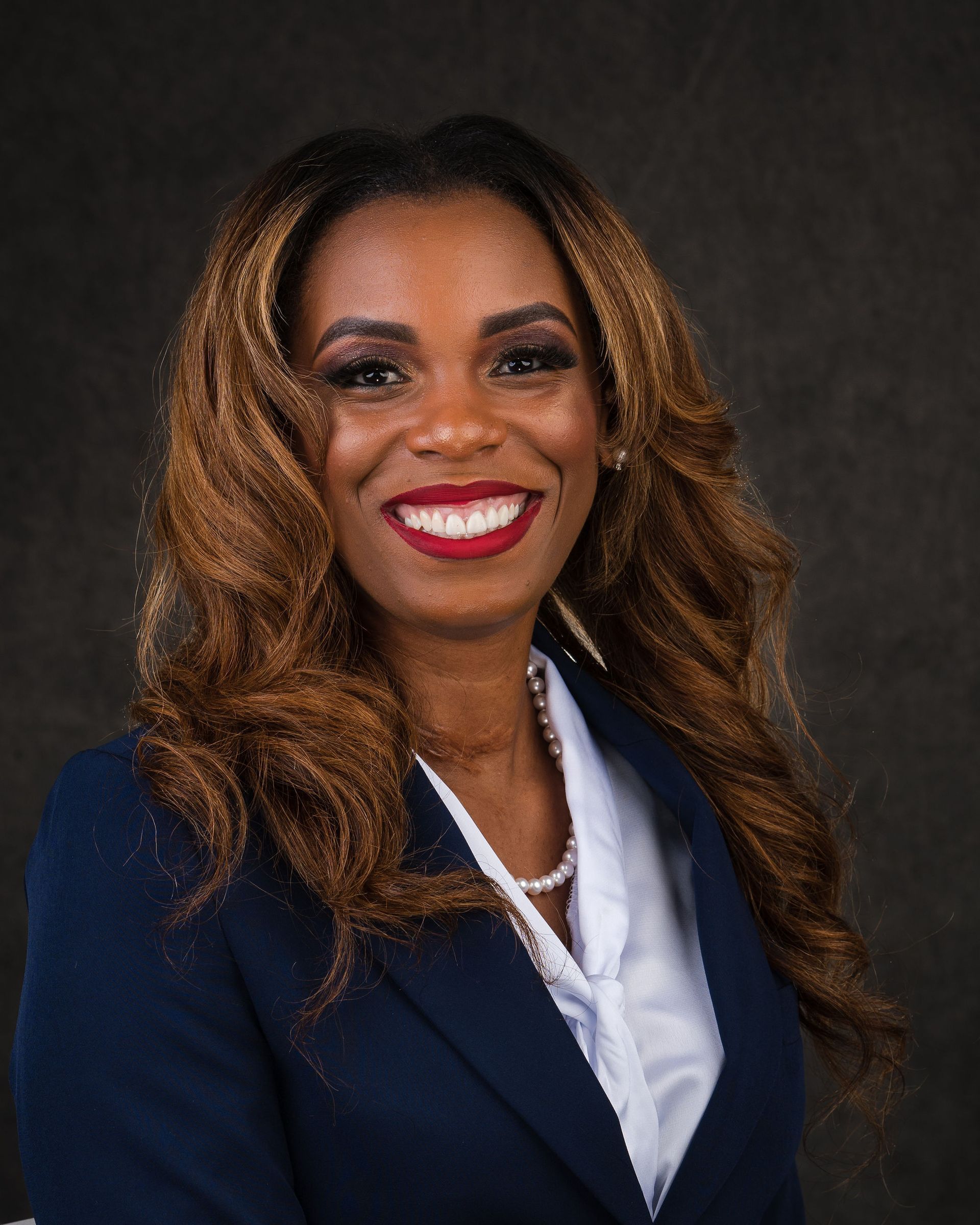 Portrait of a smiling woman in a navy blazer and white blouse against a dark background