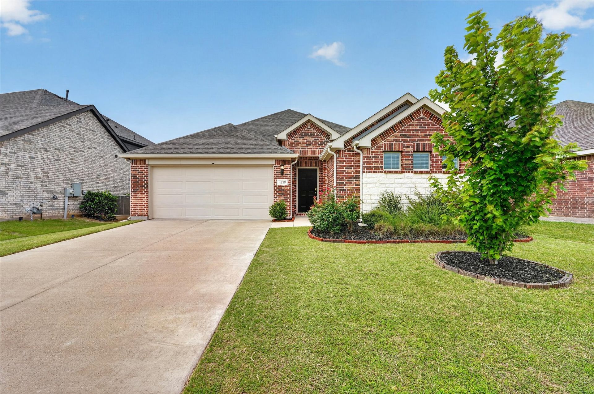 Suburban brick house with two-car garage, driveway, and manicured lawn
