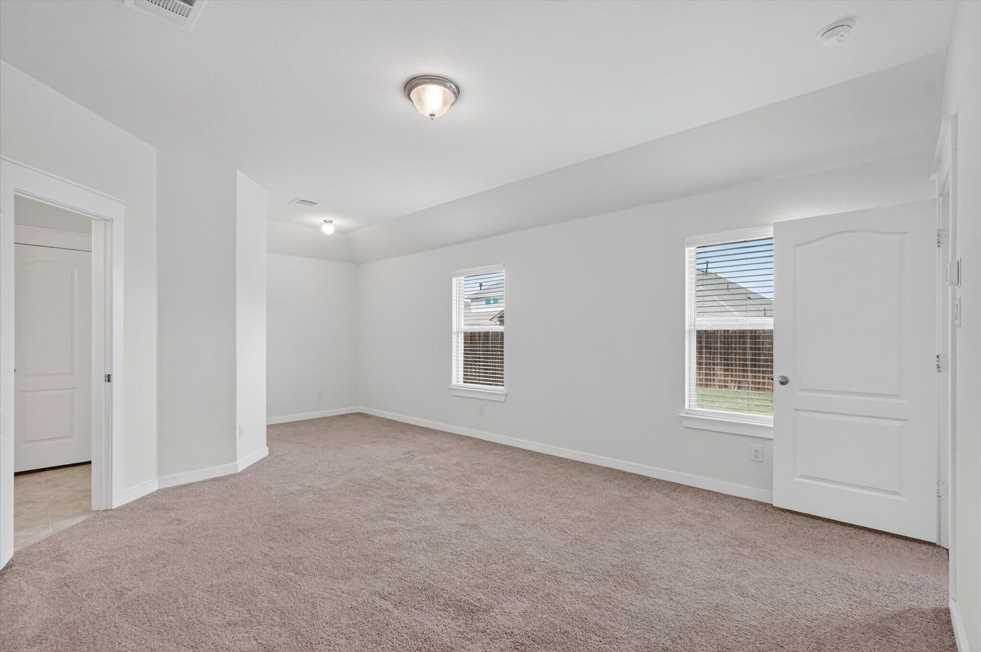 Empty carpeted bedroom with white walls, two windows, and a closet door