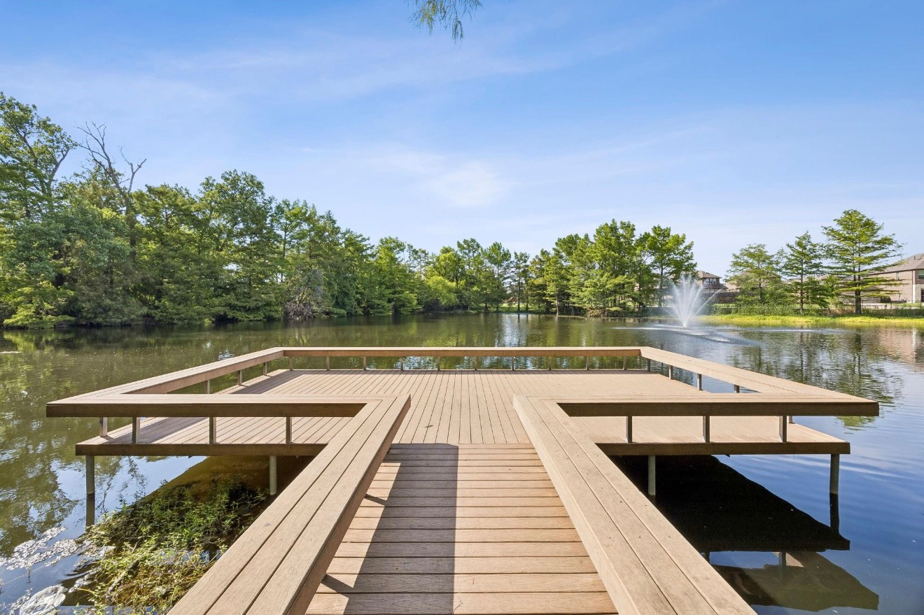 Wooden dock extending over a calm lake, surrounded by green trees under a clear blue sky.