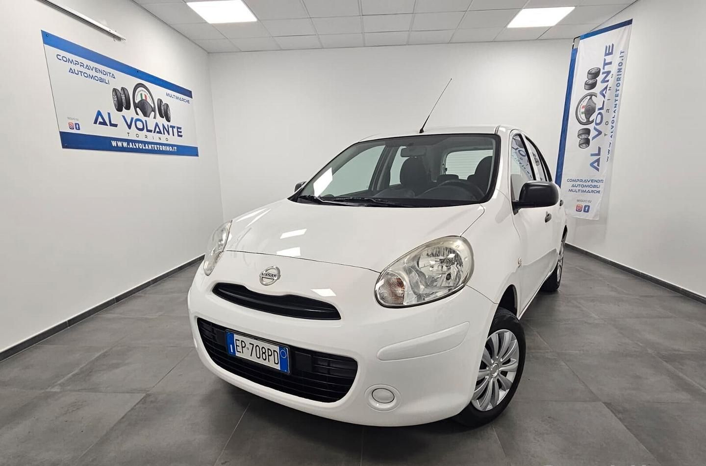 Una Opel Corsa hatchback bianca parcheggiata nello showroom interno di una concessionaria, luminoso e con pareti bianche.