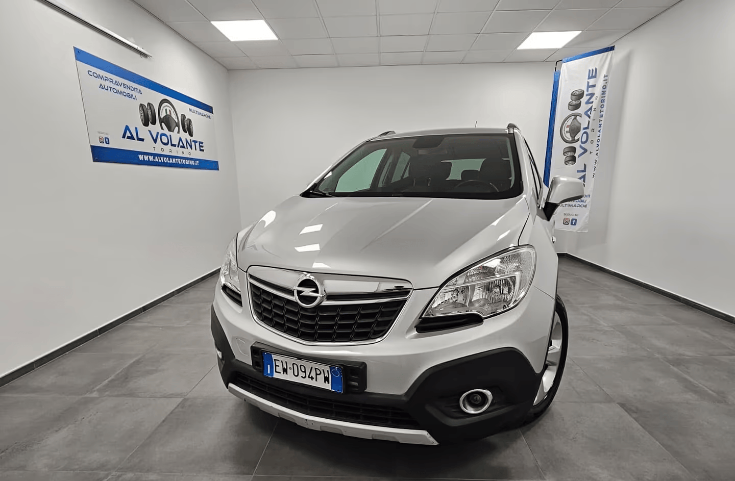 Una BMW Serie 1 hatchback color argento parcheggiata in un luminoso showroom al coperto con pavimento piastrellato e un cartello sulla parete.