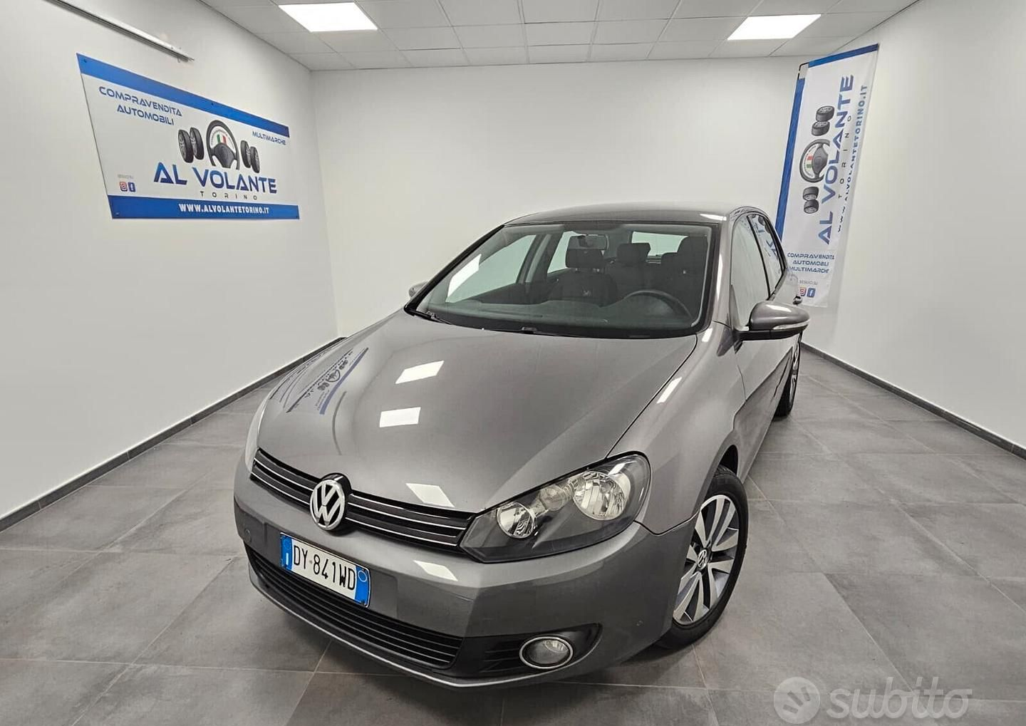 Una Renault Clio hatchback rossa parcheggiata nello showroom luminoso e moderno di una concessionaria, con pareti bianche e pavimento piastrellato.