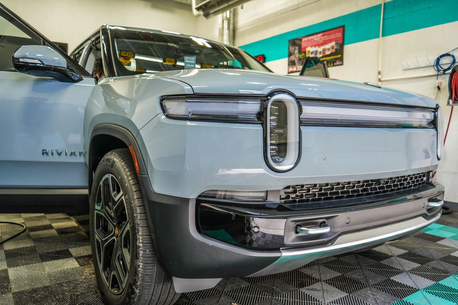Light blue Rivian electric SUV with the driver's side door open, parked inside a garage.