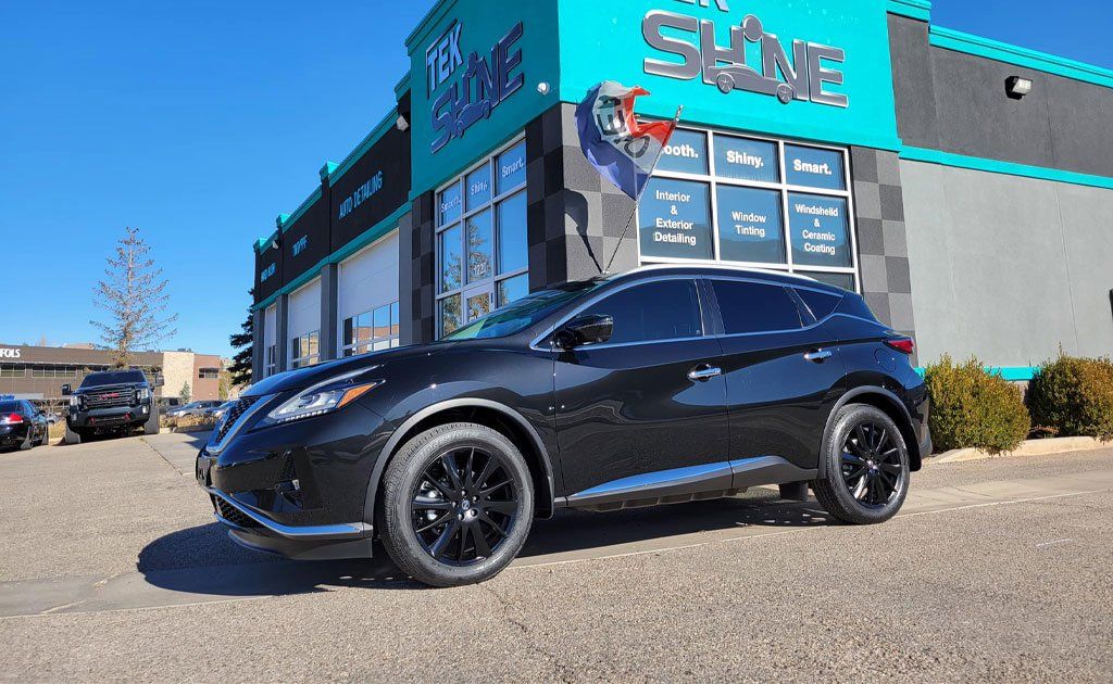 Black SUV parked in front of a car detailing business with a blue and black facade on a sunny day.
