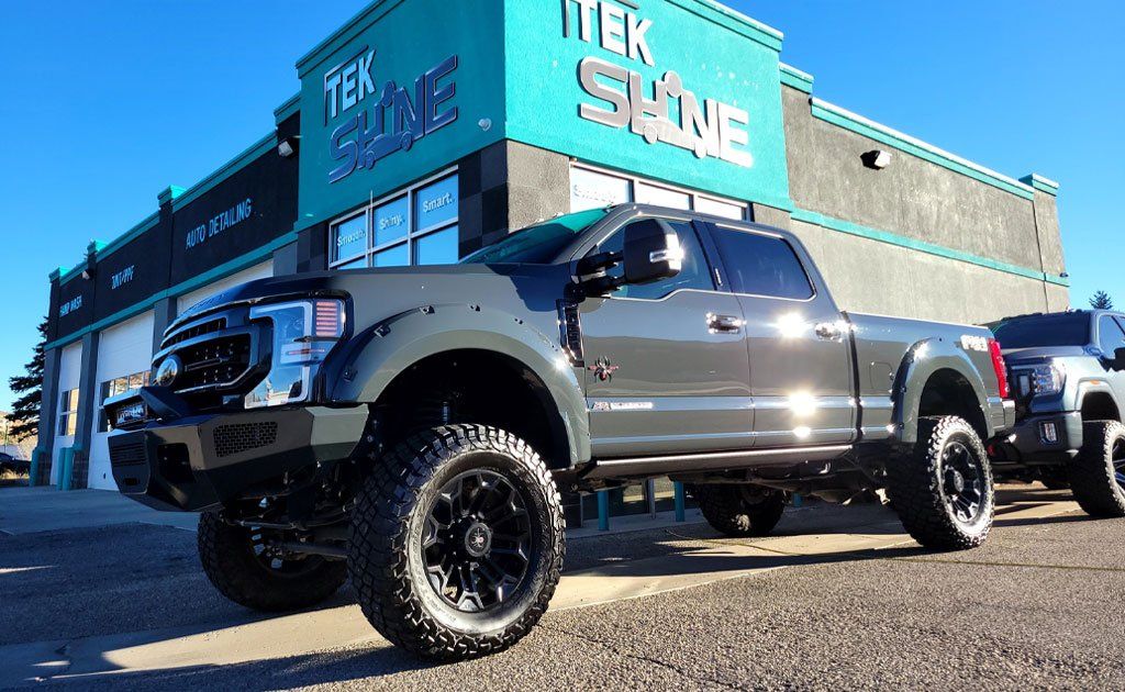 Grey lifted truck parked in front of a blue and grey building with the words