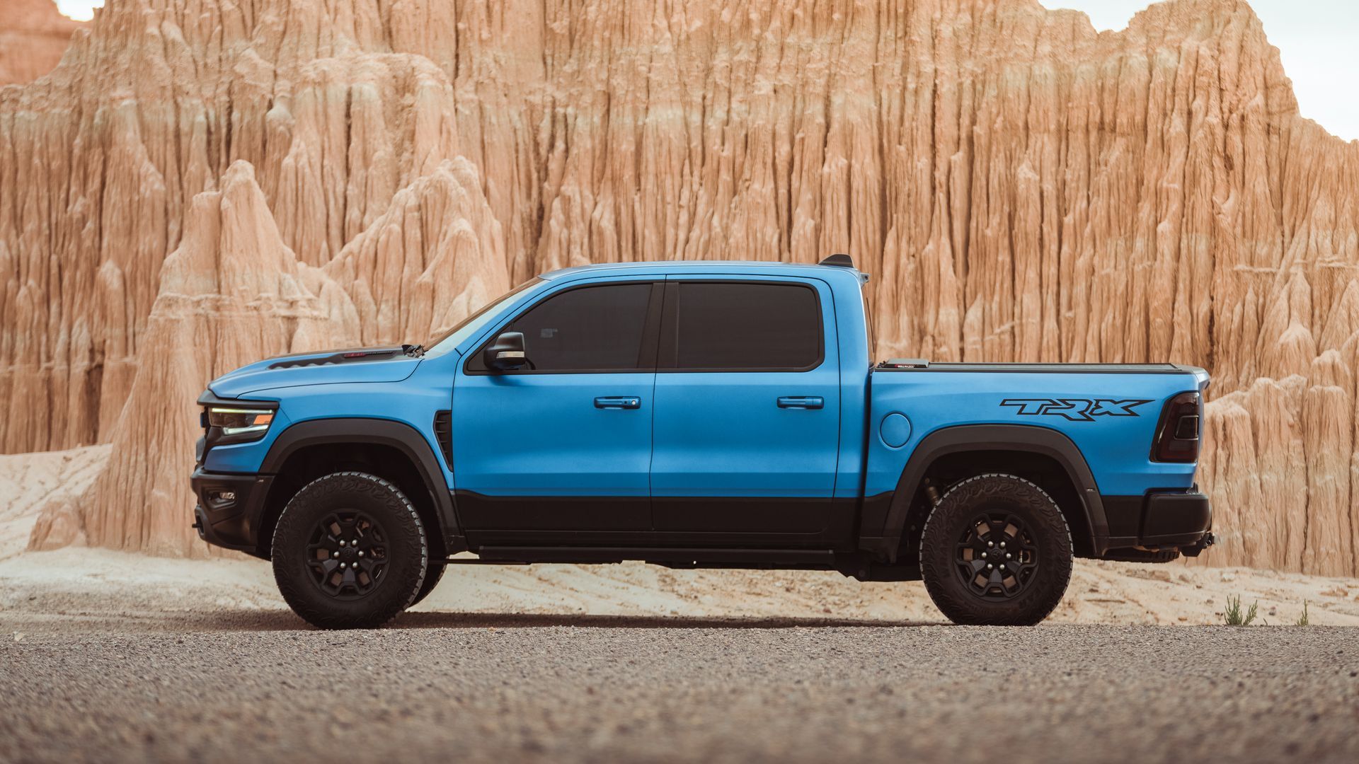 A blue ram truck is parked on the side of the road in front of a mountain.