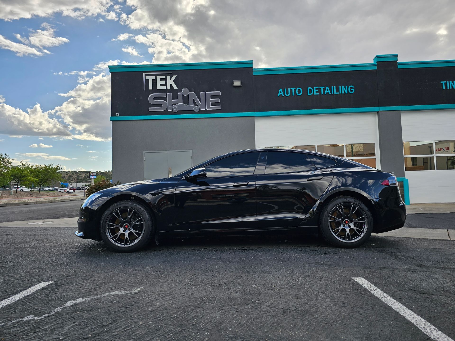 Black Tesla parked in front of Tek Shine Auto Detailing shop; cloudy sky.