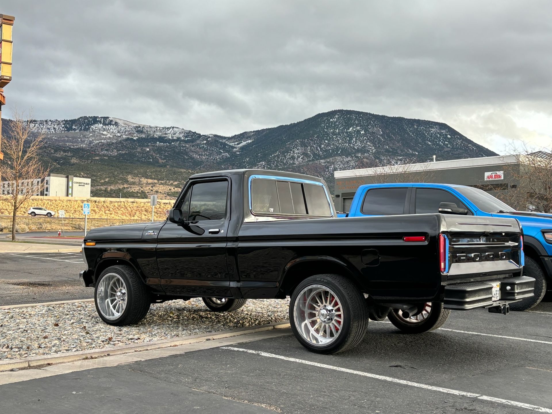 Black classic pickup truck parked outdoors with mountain backdrop.