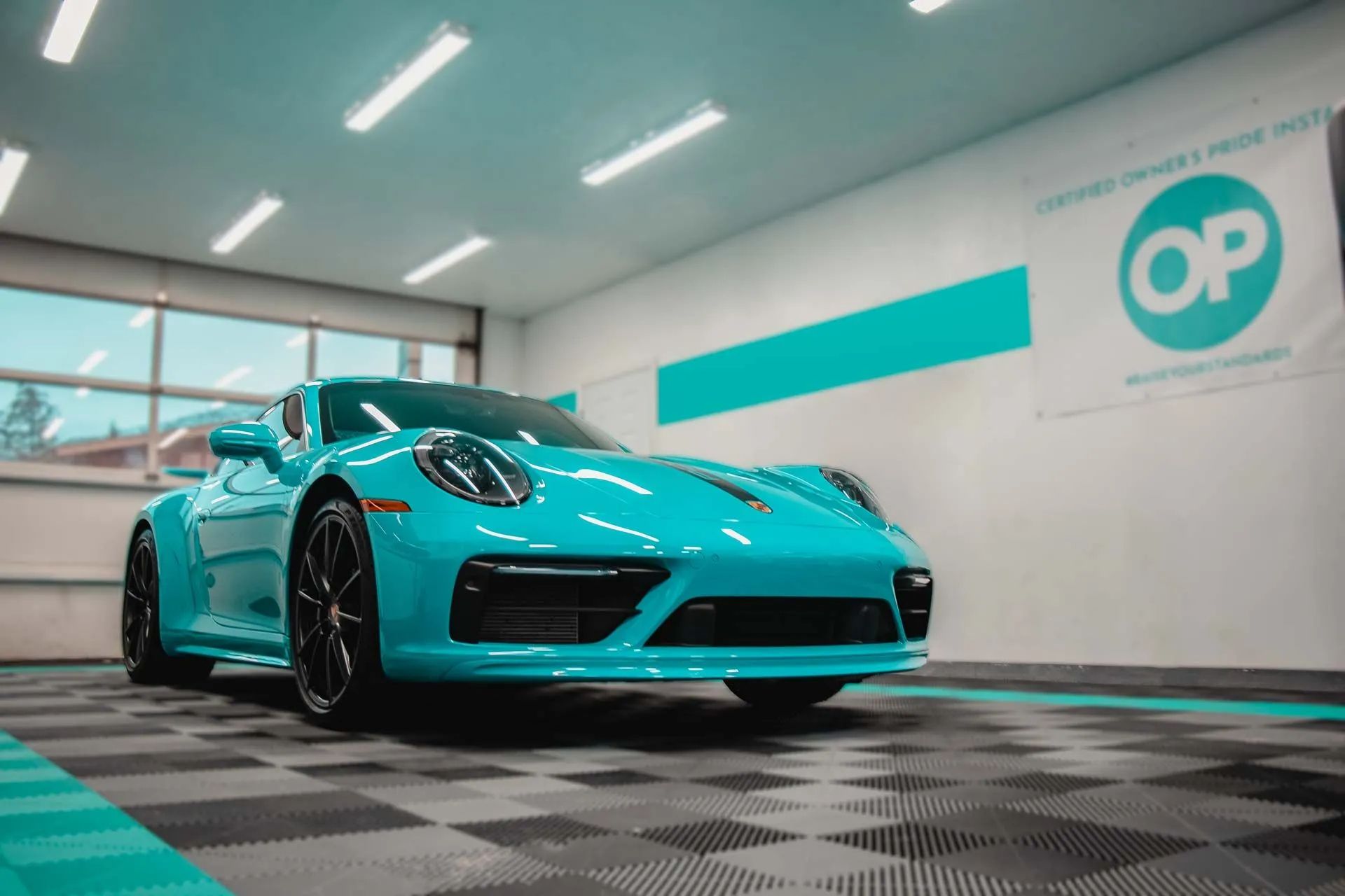 Turquoise Porsche 911 in a detail shop; black wheels, checkered floor, aqua accents.