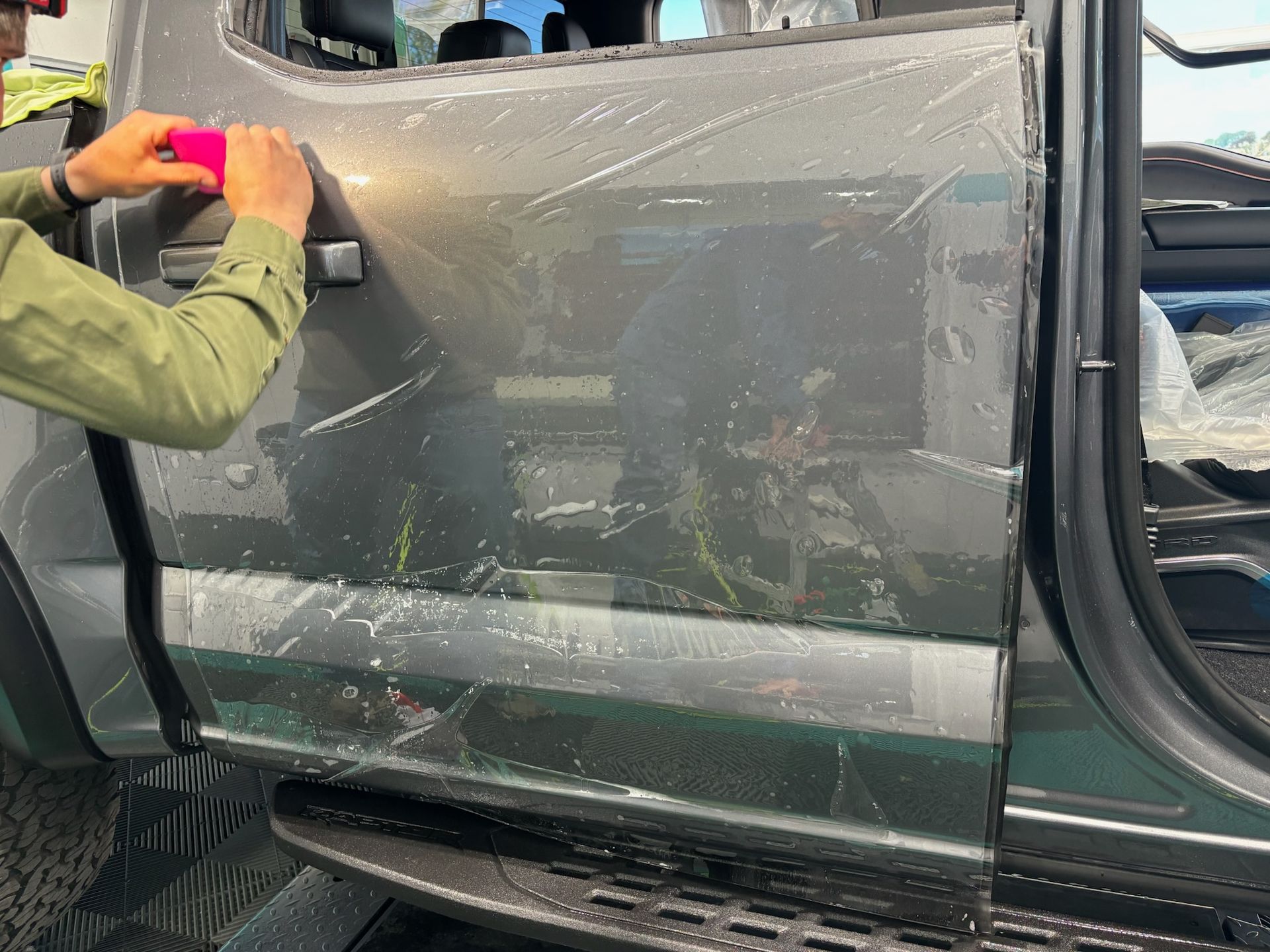 Person applying clear protective film to the door of a grey truck with a squeegee.