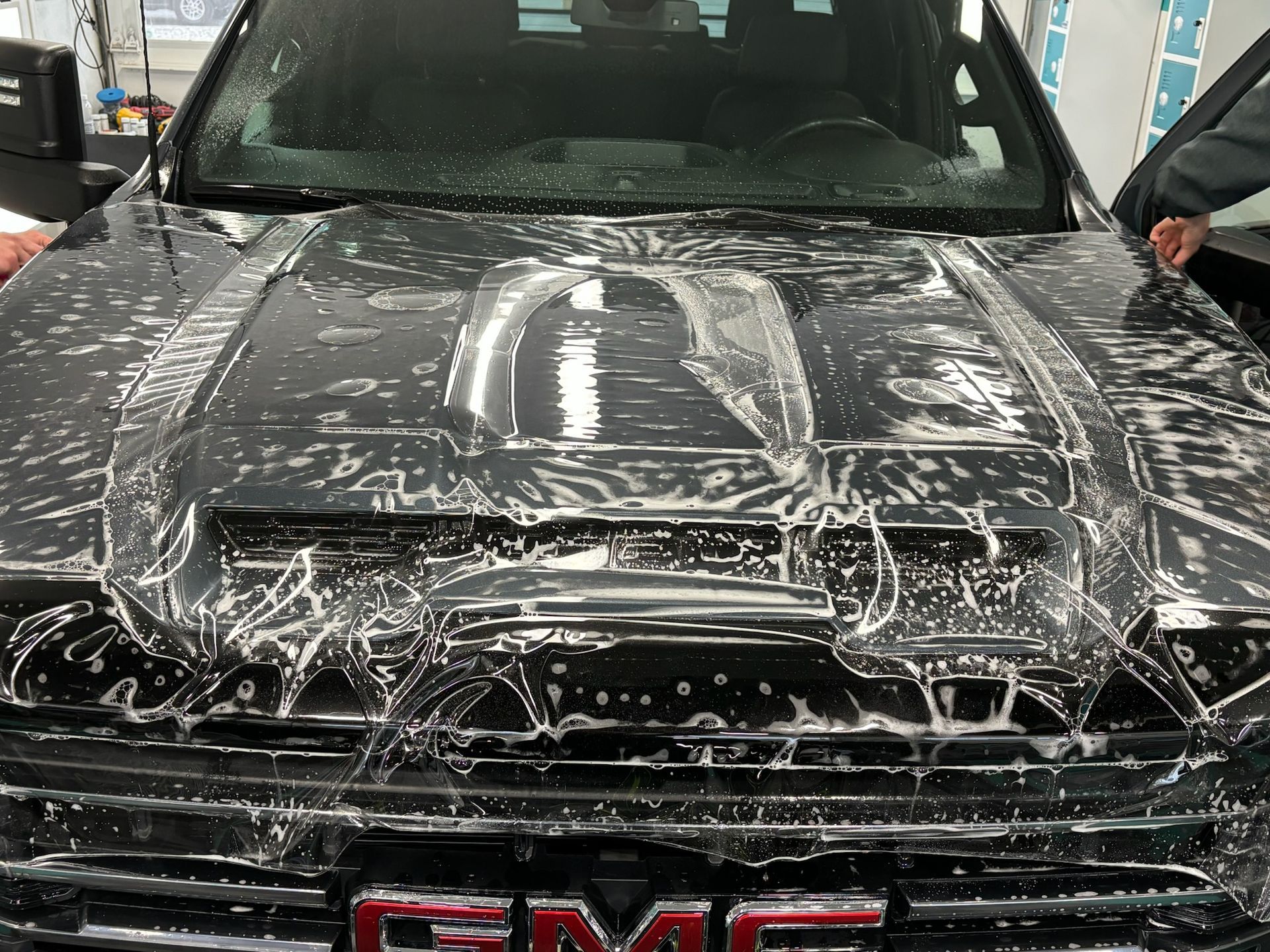Black GMC truck hood being covered in protective film by a person's hands.