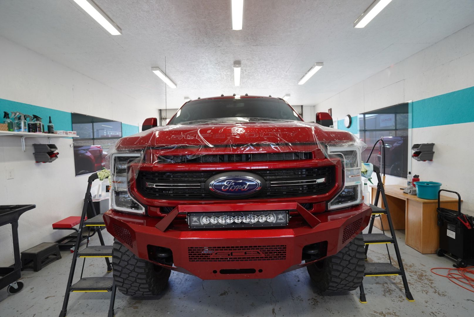 Red pickup truck in a bright auto shop, viewed head-on with tools and workbenches on both sides