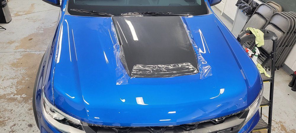 Blue sports car with black hood panel in an auto shop, front view