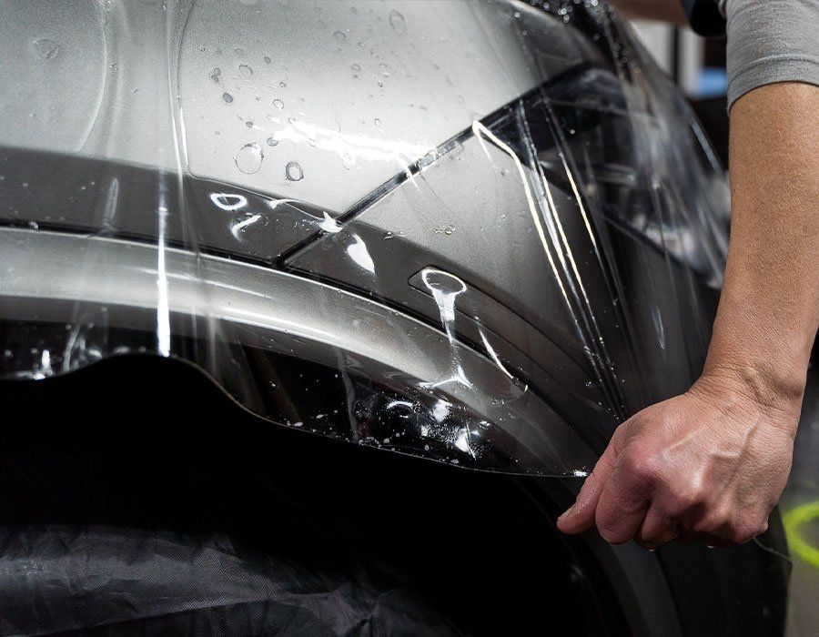 Person applying clear protective film to a silver car bumper with a squeegee