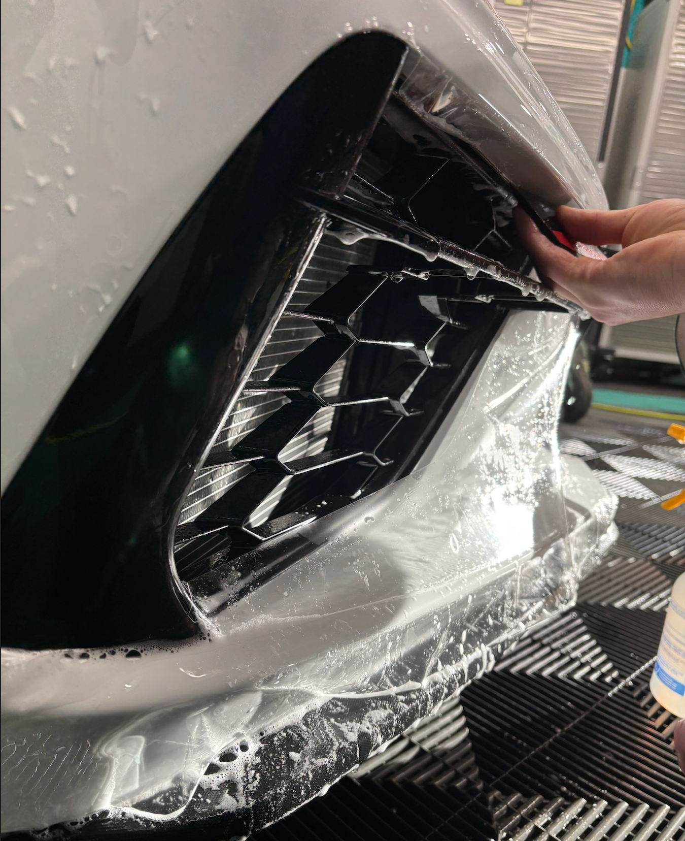 A person is applying Paint Protection Films (PPFs) the front bumper of a car