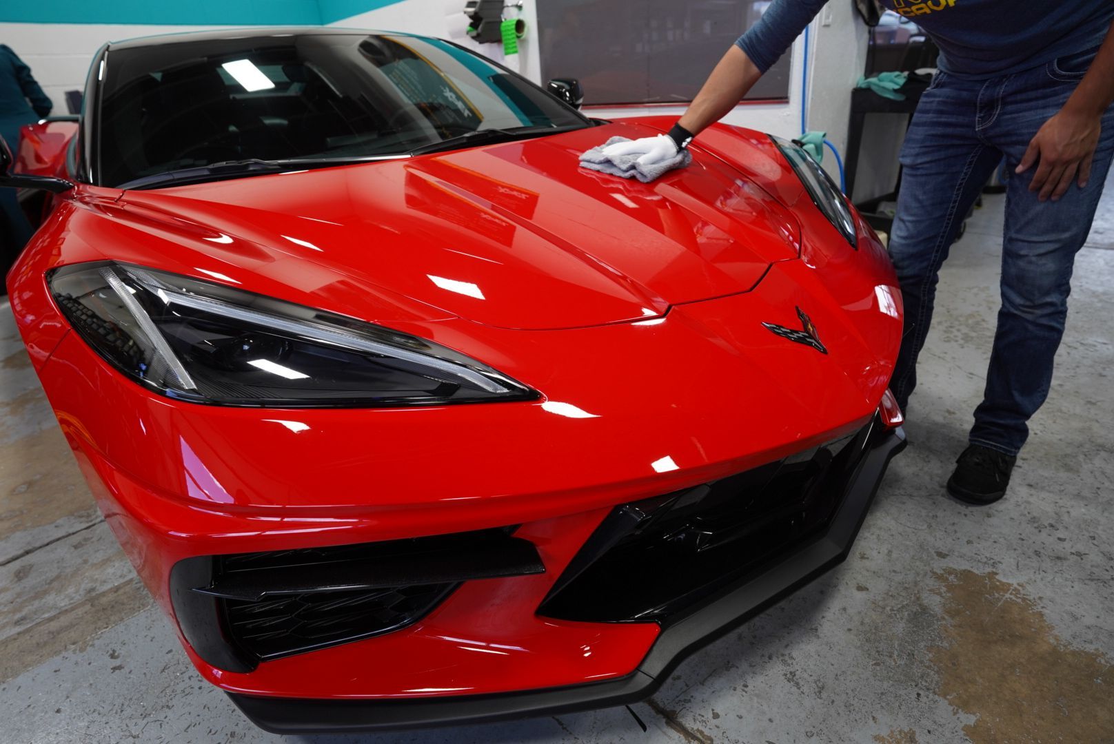 A person applying a ceramic coating to the hood of a red Corvette