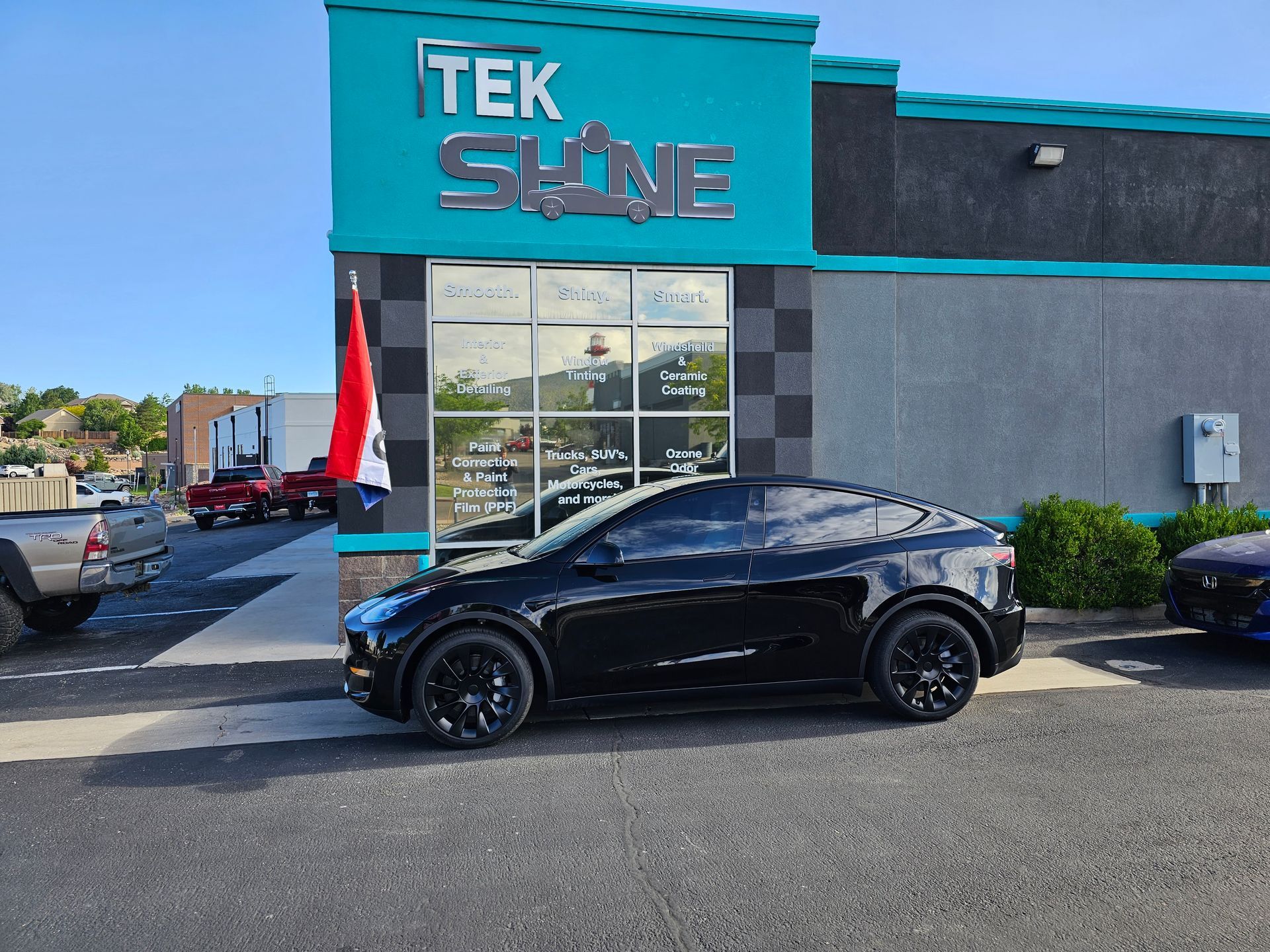 A black car is parked in front of a tek shine store.