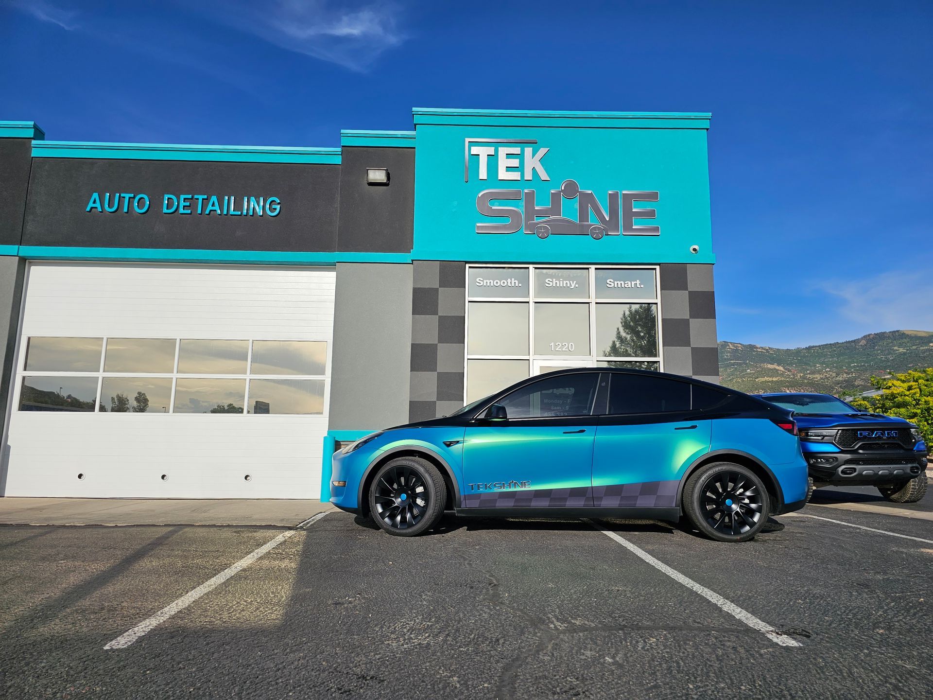 A blue car is parked in front of a tek shine auto detailing shop.