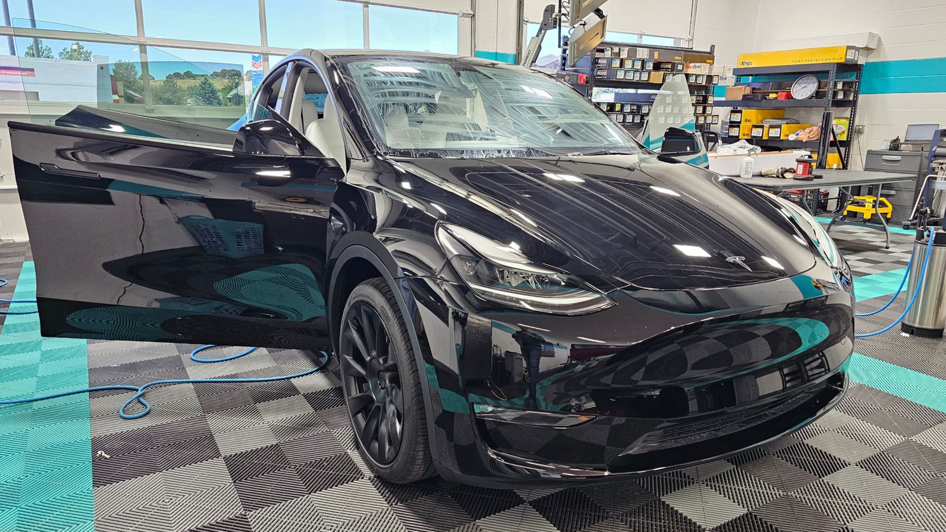 Black Tesla Model Y with open driver's side door, in a detailing shop.