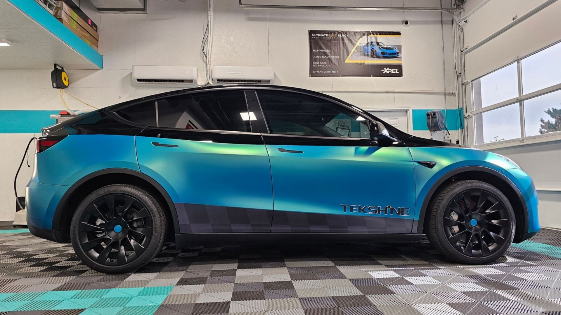 Tesla Model Y with a blue and black wrap in a garage.