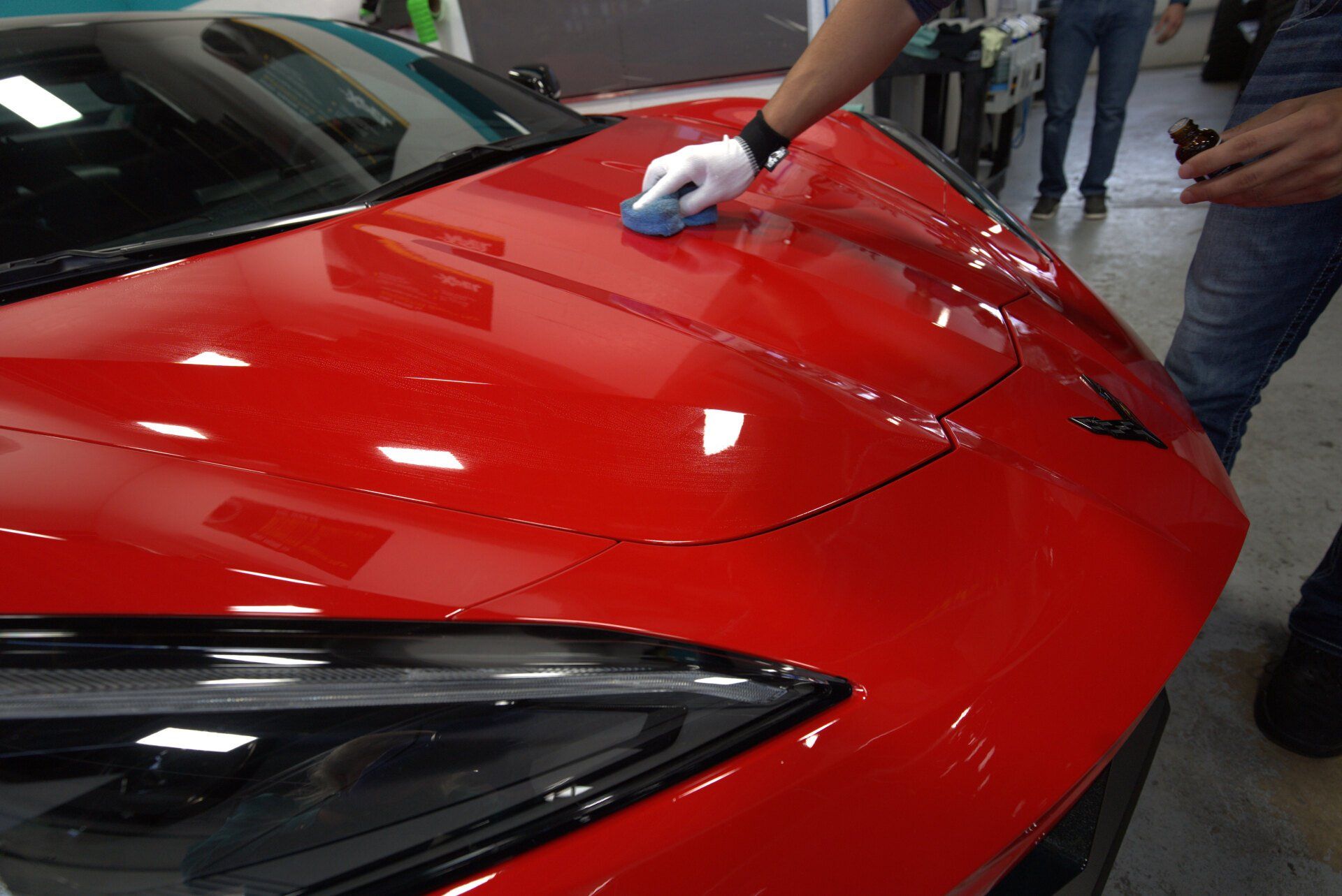 A person is polishing the hood of a red sports car.