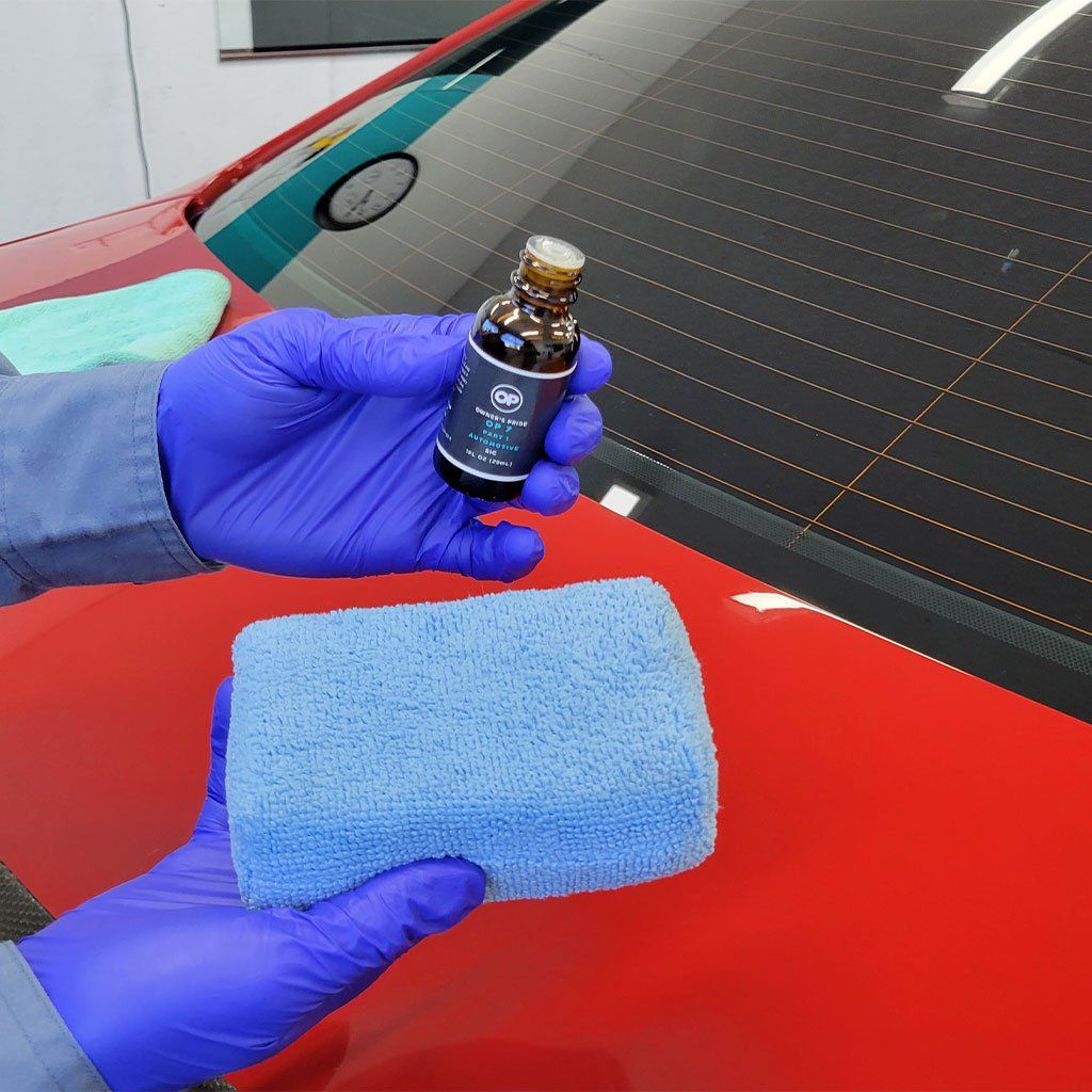 A person wearing blue gloves is holding a bottle and a sponge in front of a red car