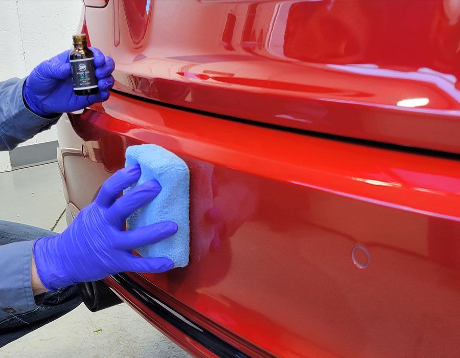 Gloved hands polishing a red car bumper with a blue cloth and small detailing tool