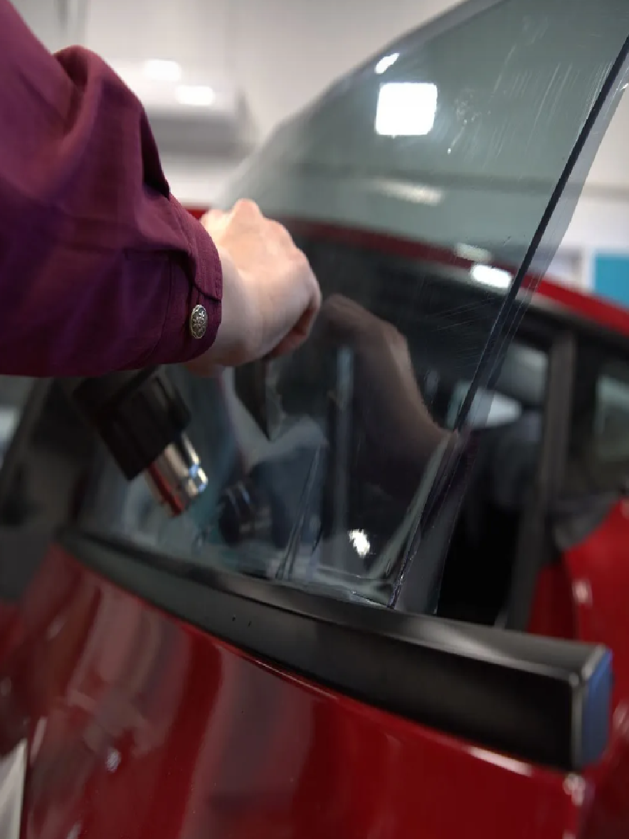 Applying heat to install window tint on a red car.